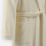 Close-up of a cream terry cloth bathrobe showing the tie belt and front pocket detail.