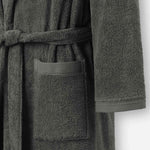 Close-up of a dark grey terry cotton bathrobe showing the waist tie belt, front patch pocket, and sleeve cuff detail.