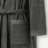 Close-up of a dark grey terry cotton bathrobe showing the waist tie belt, front patch pocket, and sleeve cuff detail.