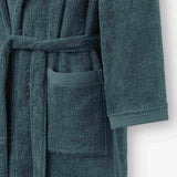 Close-up of a teal terry cotton bathrobe showing the waist tie belt, front patch pocket, and sleeve cuff detail.