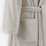 Close-up of a cream terry cloth bathrobe showing the waist tie belt, front patch pocket, and sleeve cuff detail.