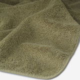 Close-up of a dark olive cotton towel highlighting the soft terry texture, rounded corner finish, and subtle embroidered logo detail.