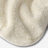 Close-up of a light cream cotton towel highlighting the soft terry texture, rounded corner finish, and subtle embroidered logo detail.