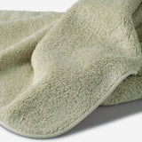 Close-up of a sage green cotton towel highlighting the soft terry texture, rounded corner finish, and subtle embroidered logo detail.