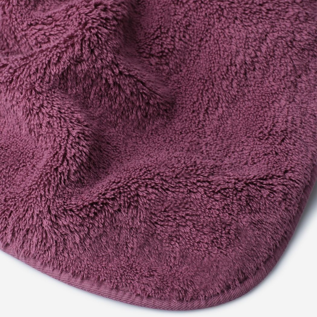 Close-up of a pruple cotton towel highlighting the soft terry texture, rounded corner finish, and subtle embroidered logo detail.