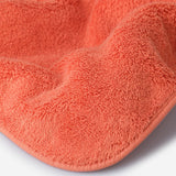 Close-up of an orange cotton towel highlighting the soft terry texture, rounded corner finish, and subtle embroidered logo detail.
