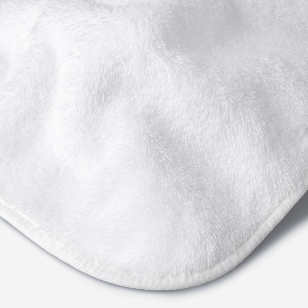 Close-up of a white cotton towel highlighting the soft terry texture, rounded corner finish, and subtle embroidered logo detail.