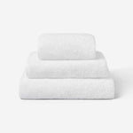 Stack of three white cotton towels in different sizes, neatly folded and placed on a white background.