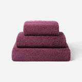 Stack of three plum cotton towels in different sizes, featuring a plush and soft texture against a white background.