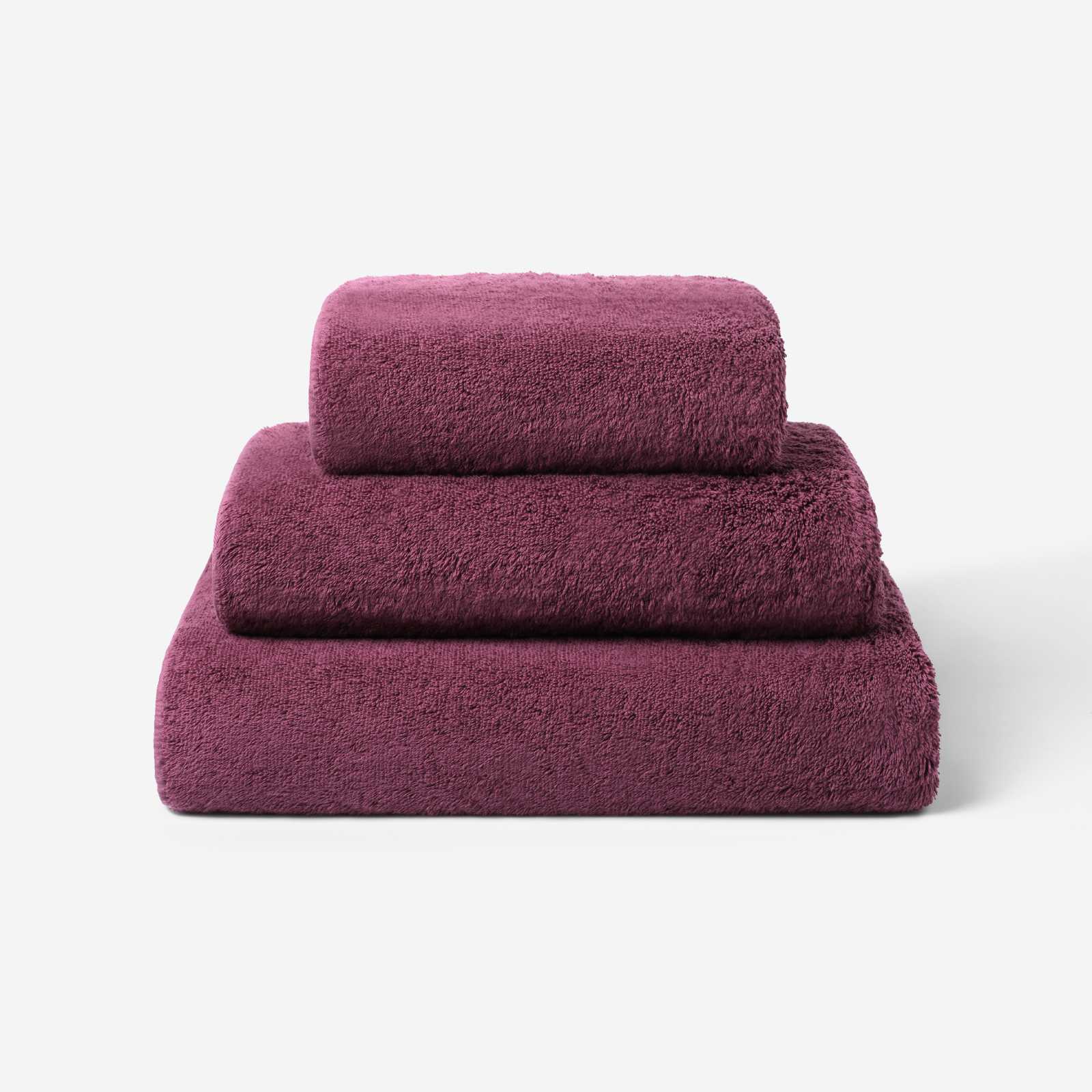 Stack of three plum cotton towels in different sizes, featuring a plush and soft texture against a white background.