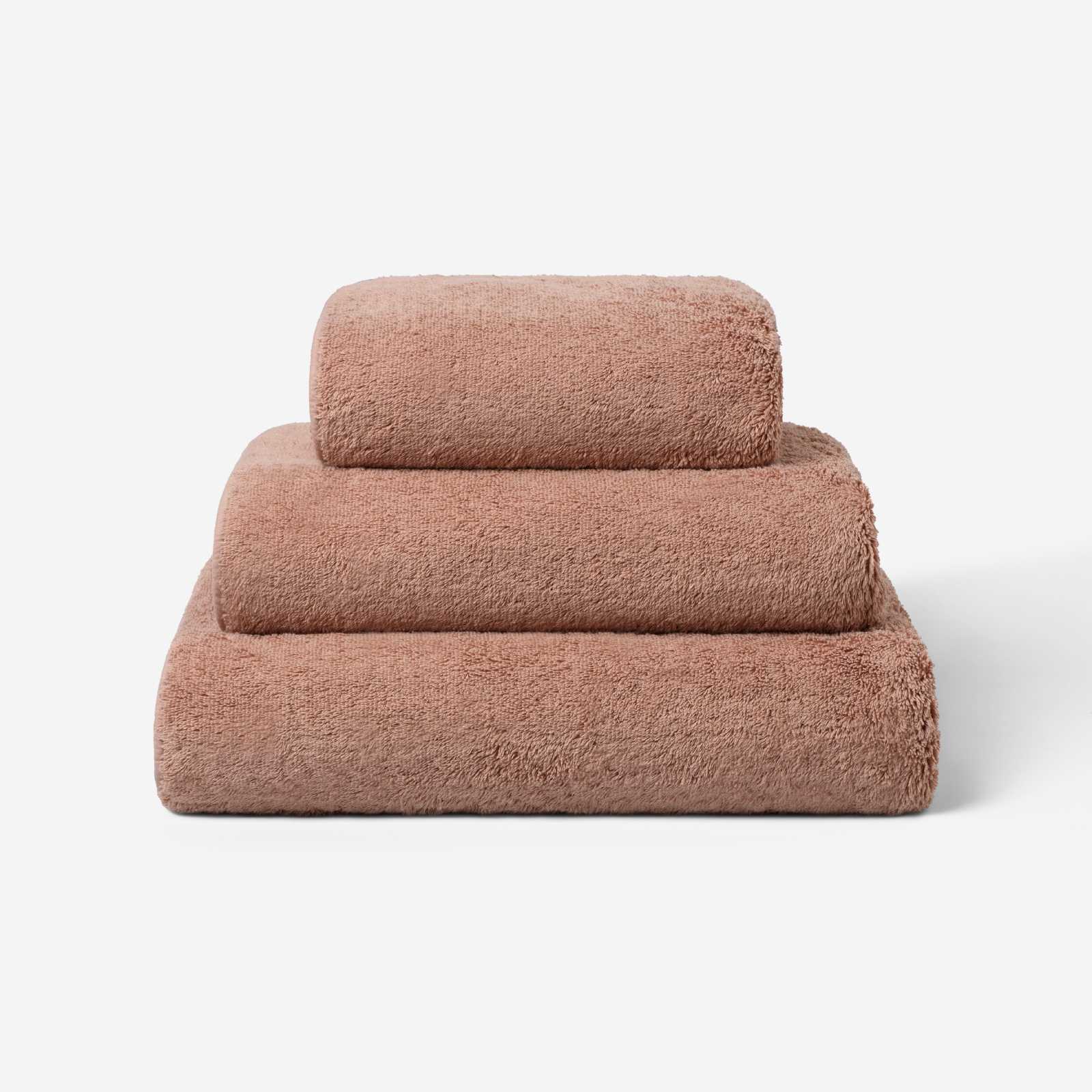 Stack of three dusty rose luxury cotton towels in different sizes, featuring a plush soft texture against a neutral background.