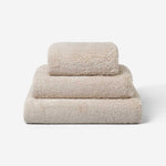 Stack of three beige cotton towels in different sizes, neatly folded and placed on a white background.