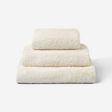 Stack of three light cream cotton towels in different sizes, neatly folded and placed on a white background.
