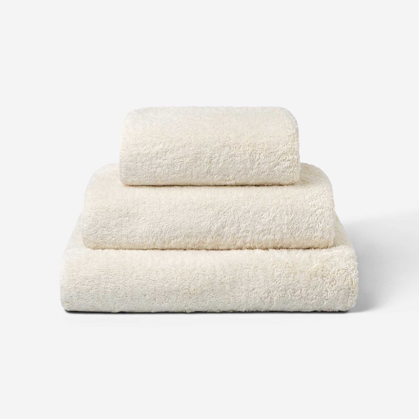 Stack of three light cream cotton towels in different sizes, neatly folded and placed on a white background.