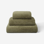 Stack of three dark olive green towels in different sizes, neatly folded and placed on a light background, showing the terry surface texture.
