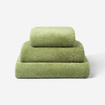 Stack of three olive green cotton towels in different sizes, neatly folded on a light background, showcasing the soft and dense terry texture.