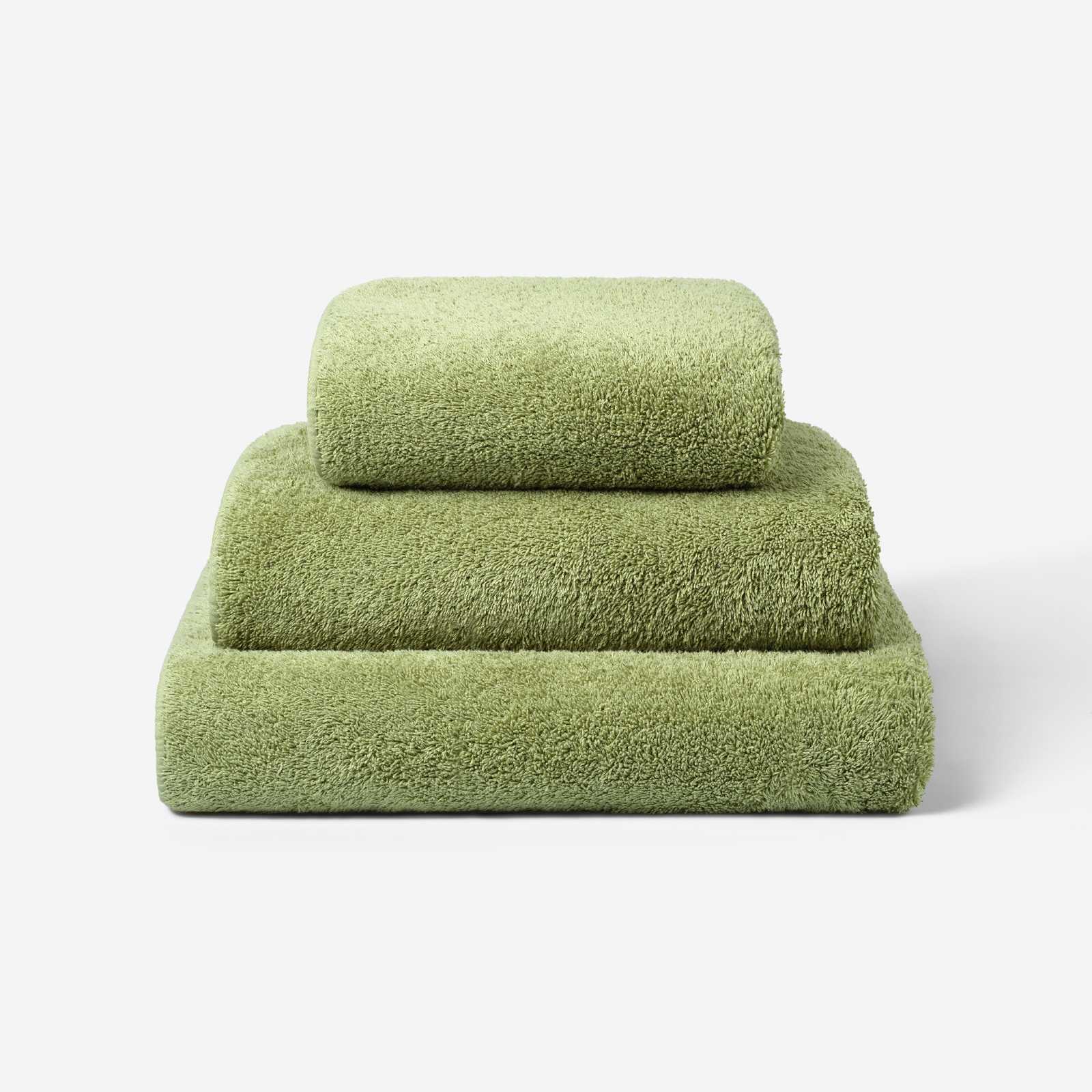 Stack of three olive green cotton towels in different sizes, neatly folded on a light background, showcasing the soft and dense terry texture.