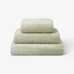 Stack of three sage green cotton towels in different sizes, neatly folded and placed on a white background.