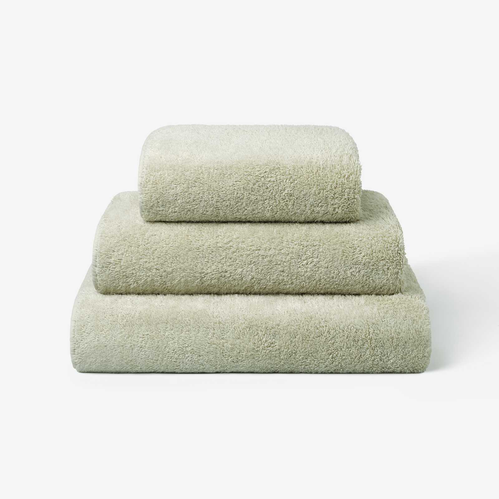 Stack of three sage green cotton towels in different sizes, neatly folded and placed on a white background.