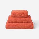 Stack of three coral cotton towels in different sizes, featuring a plush and soft texture against a white background.