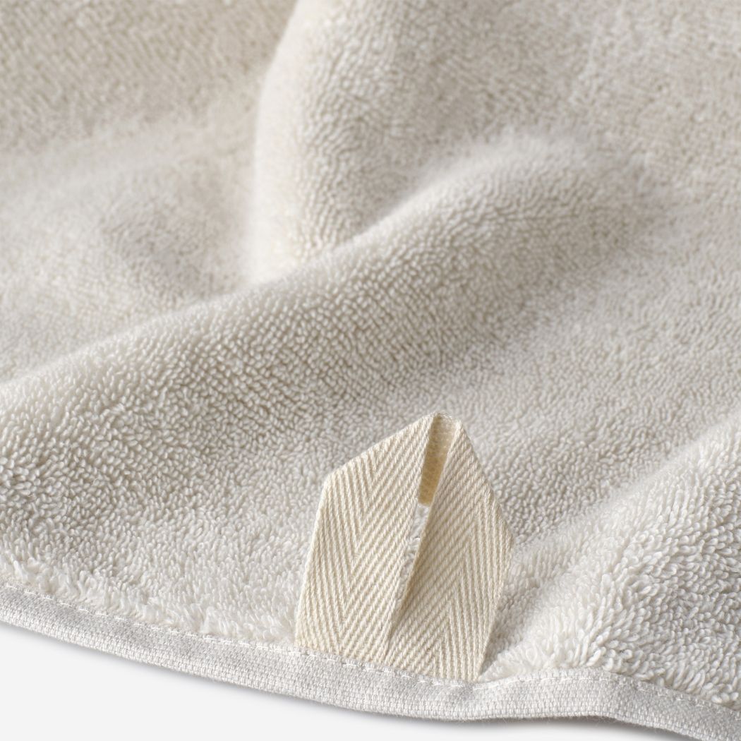 Close-up of a natural linen WATA BASIC cotton towel showing the plush terry texture and woven hanging loop detail.