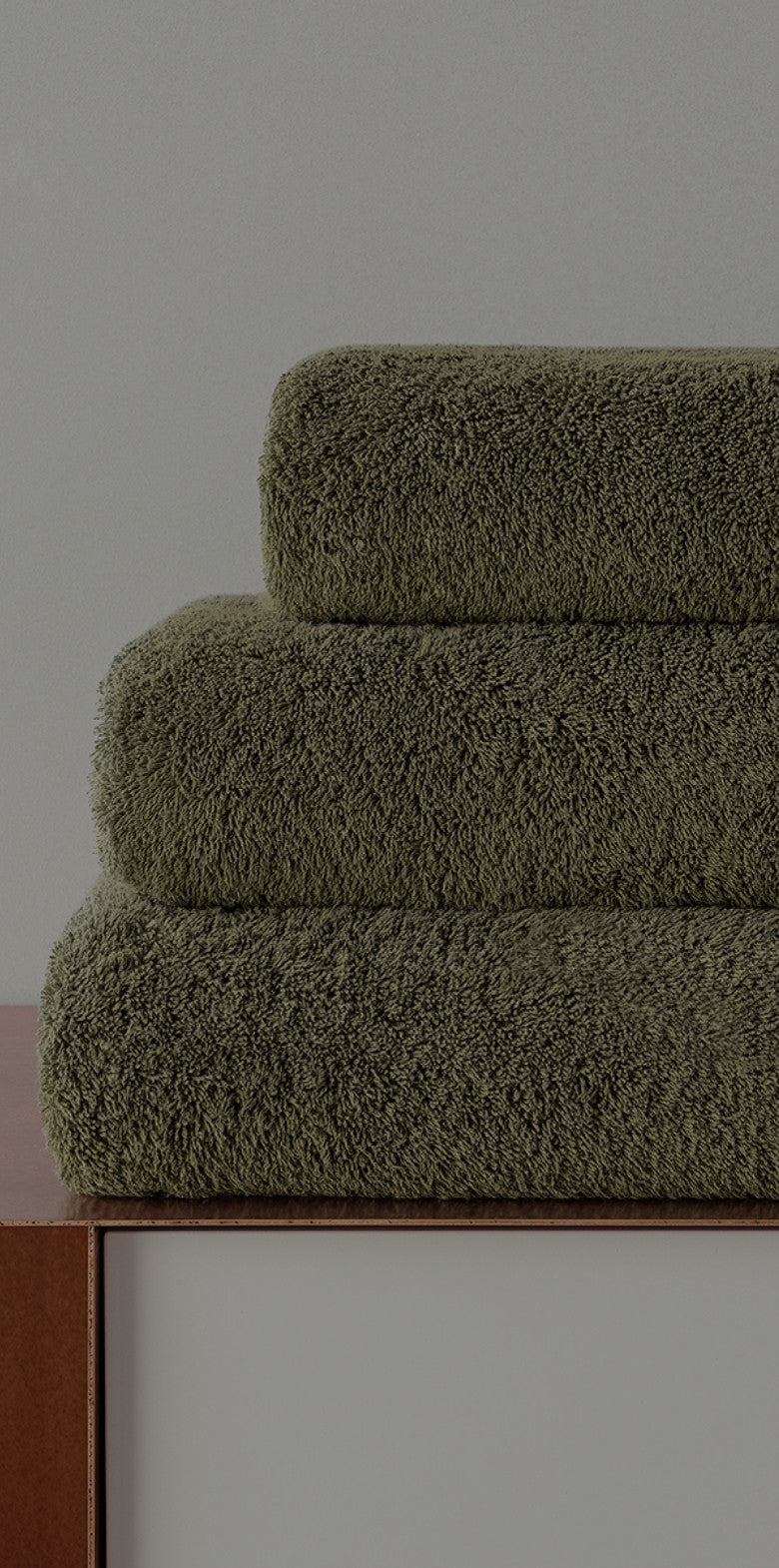 Stack of green towels on a wooden surface with a neutral background.
