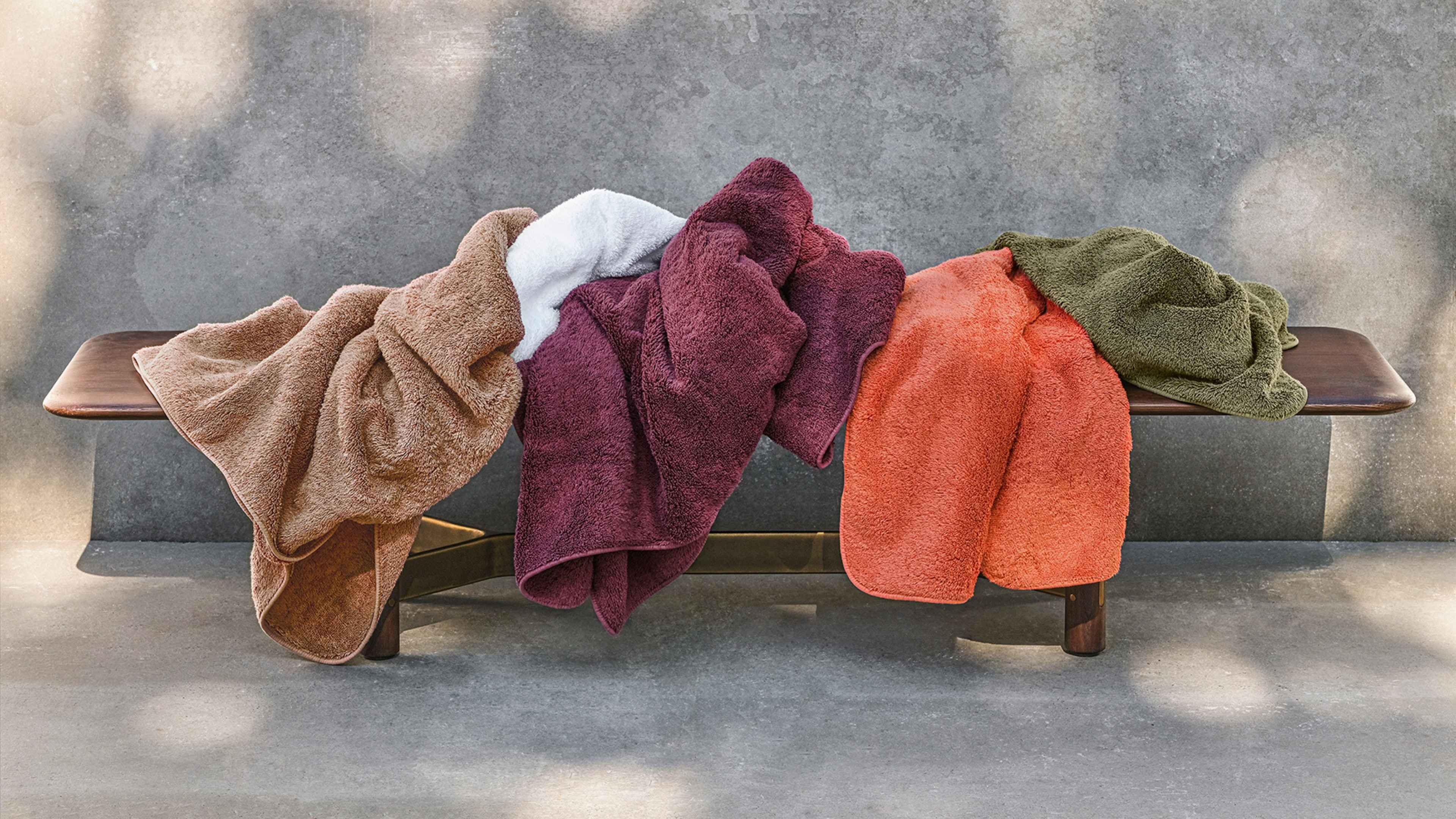 Five colorful towels draped over a wooden bench with a blurred background.
