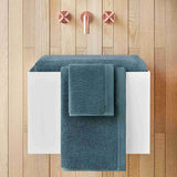 Teal towels on a white towel rack against a wooden wall with pink towel hooks.