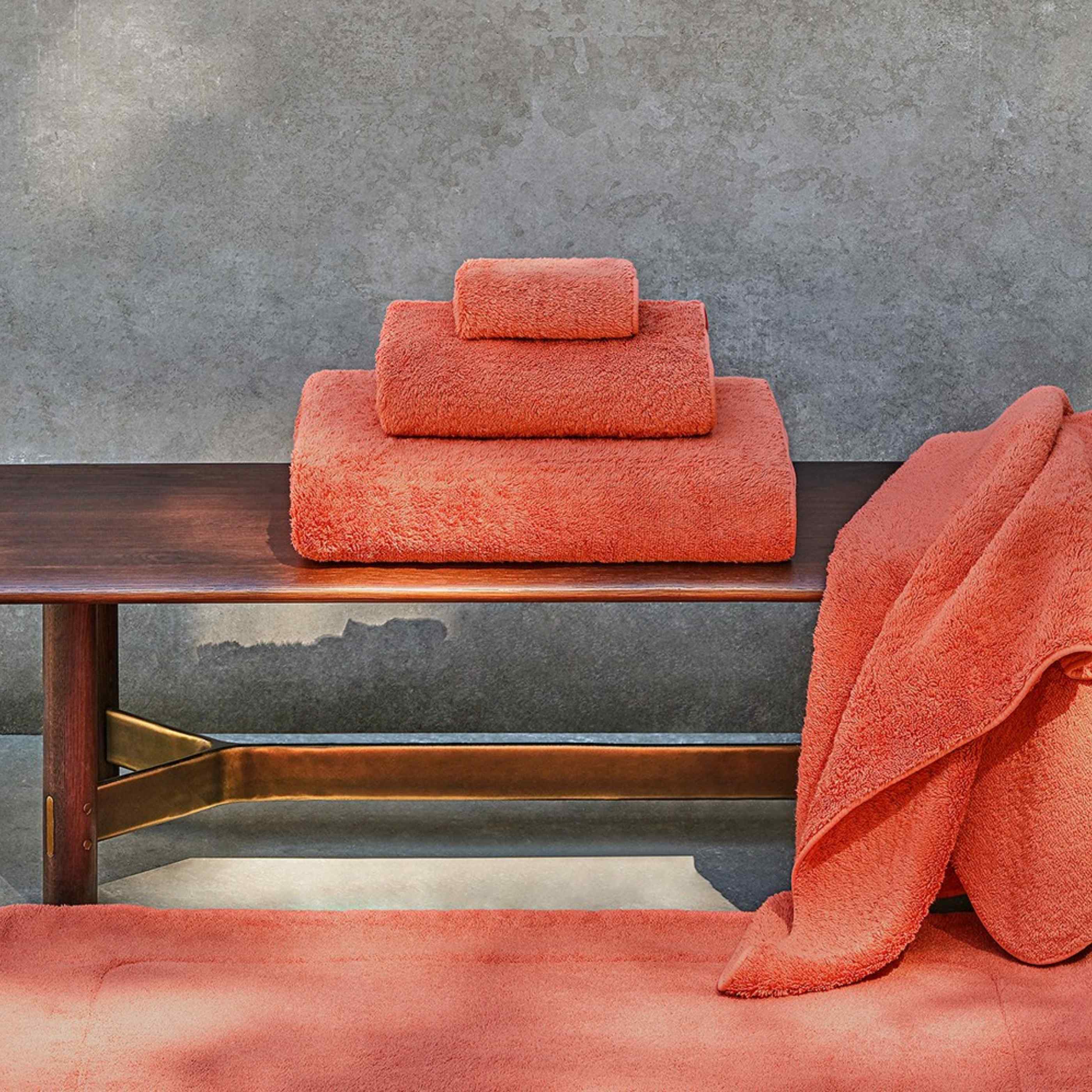 Set of orange towels on a wooden table against a gray wall.