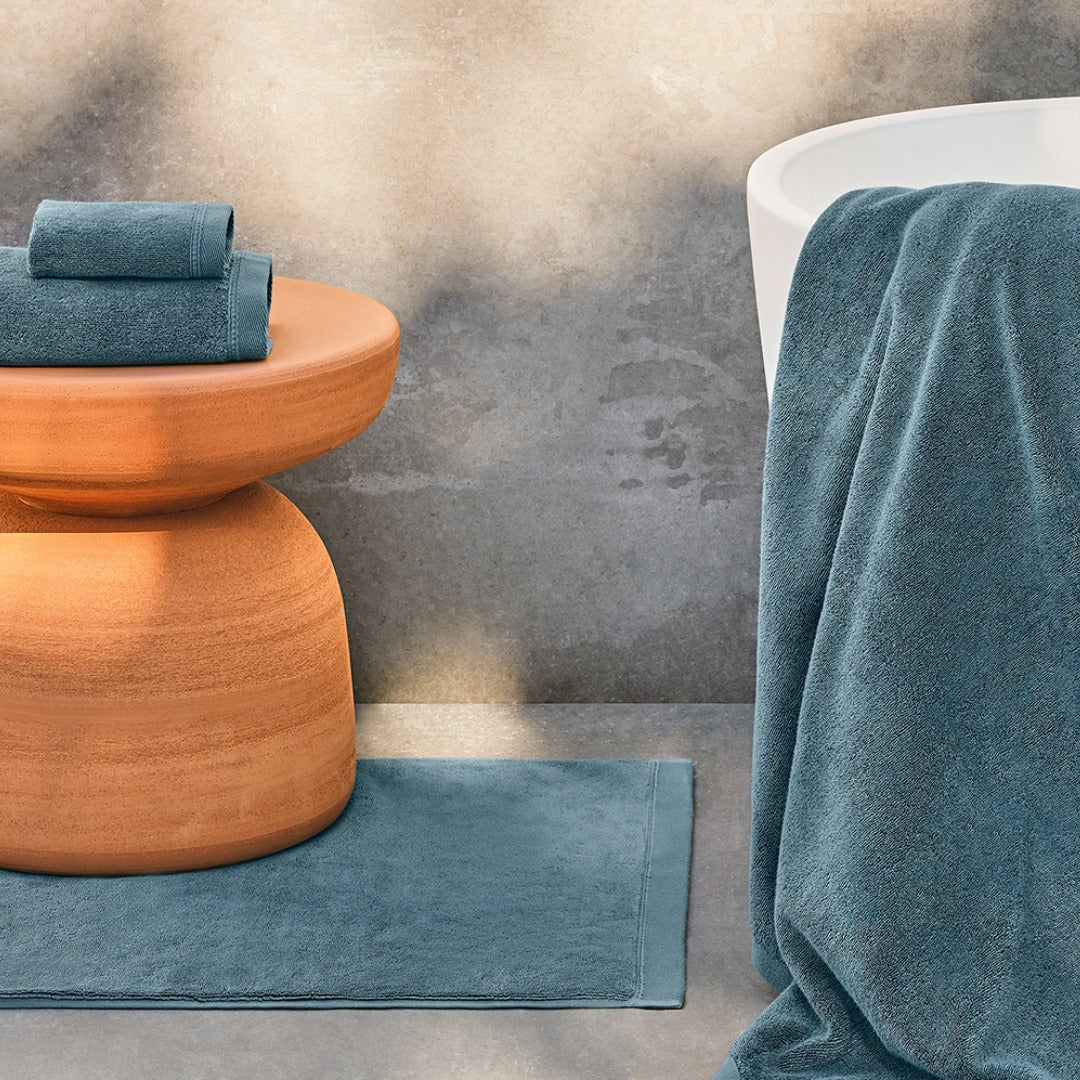 Teal bath towels displayed on a terracotta stool beside a white bathtub