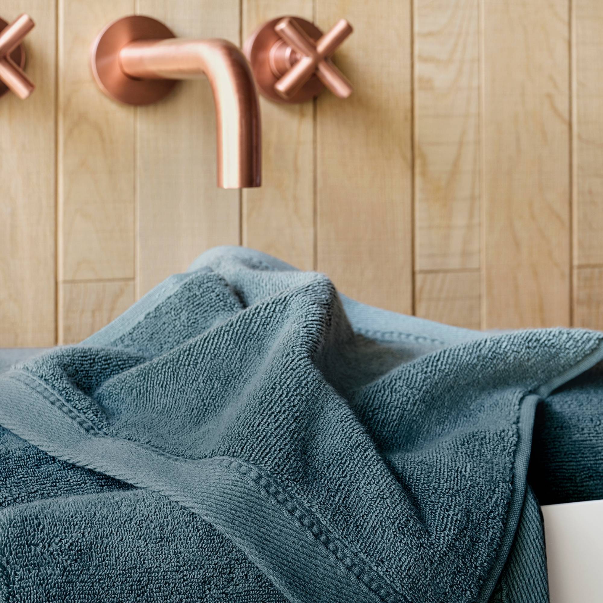 Blue towel draped over a bath tub with copper faucet and wooden wall background