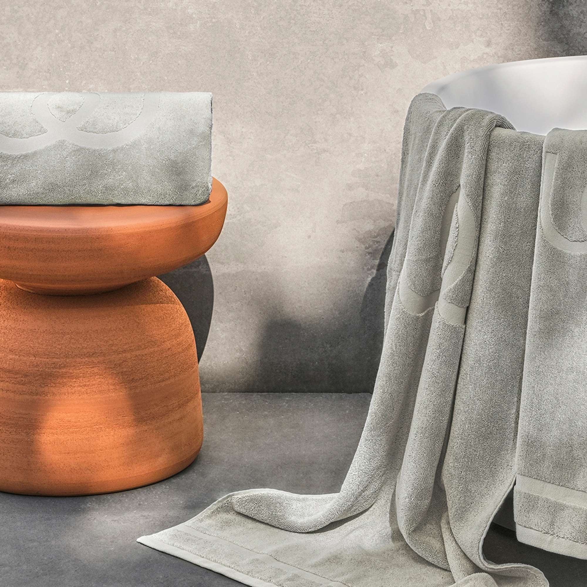 Gray towel draped over a chair next to a textured orange stool against a neutral wall.