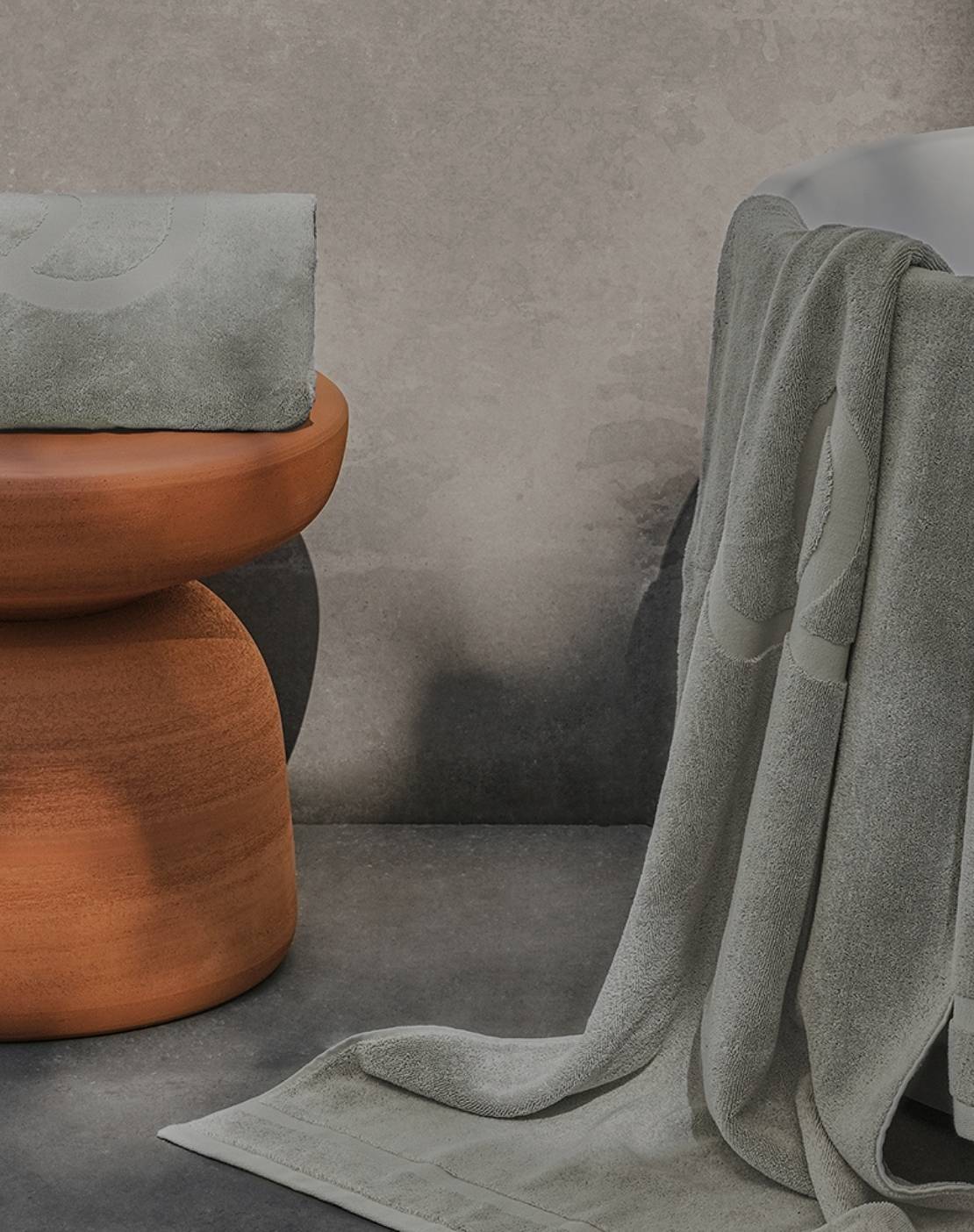 Grey Jacquard towels with logo detail, one on a clay bench and one on a bathtub