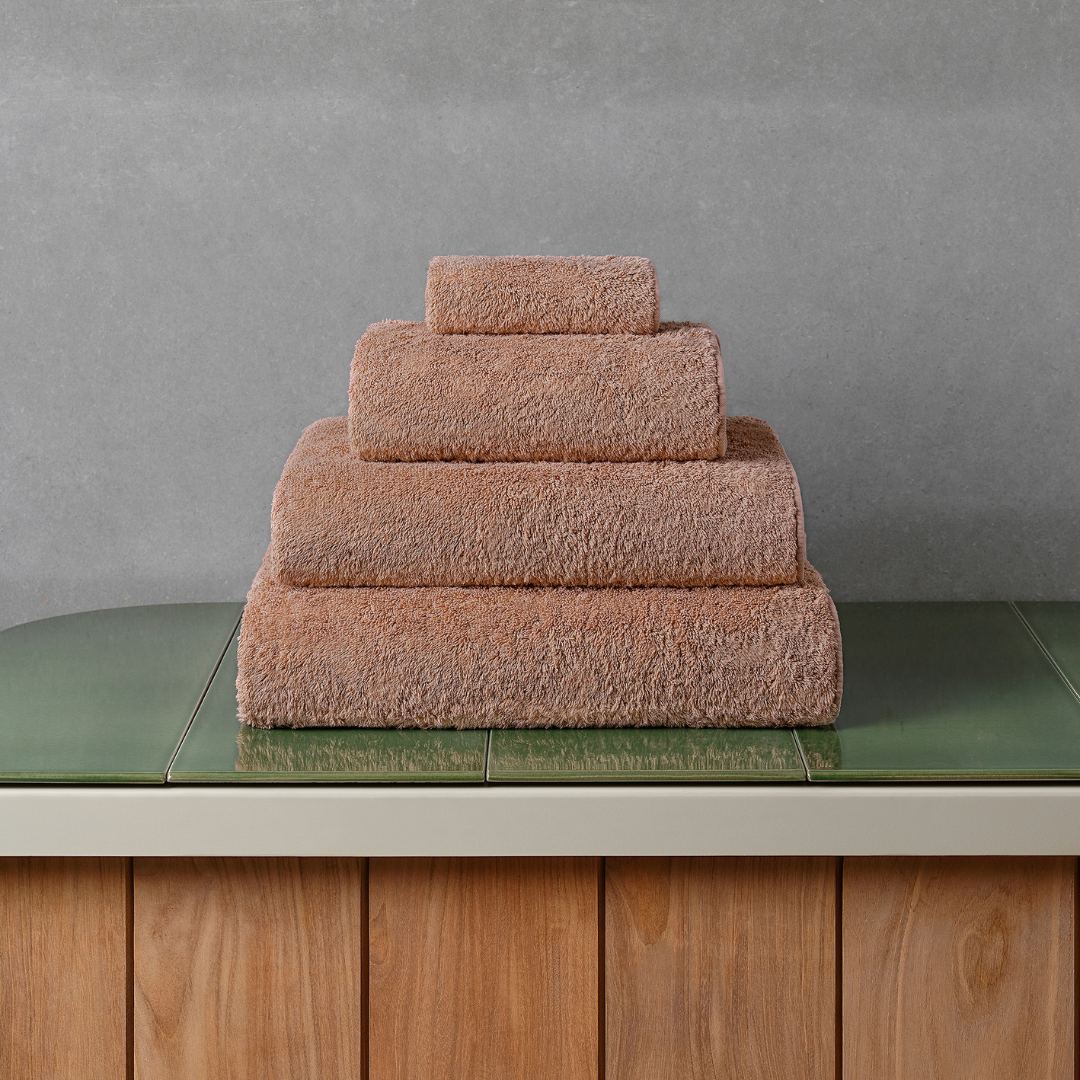 Stack of cinnamon bath towels on a green tiled bathroom counter