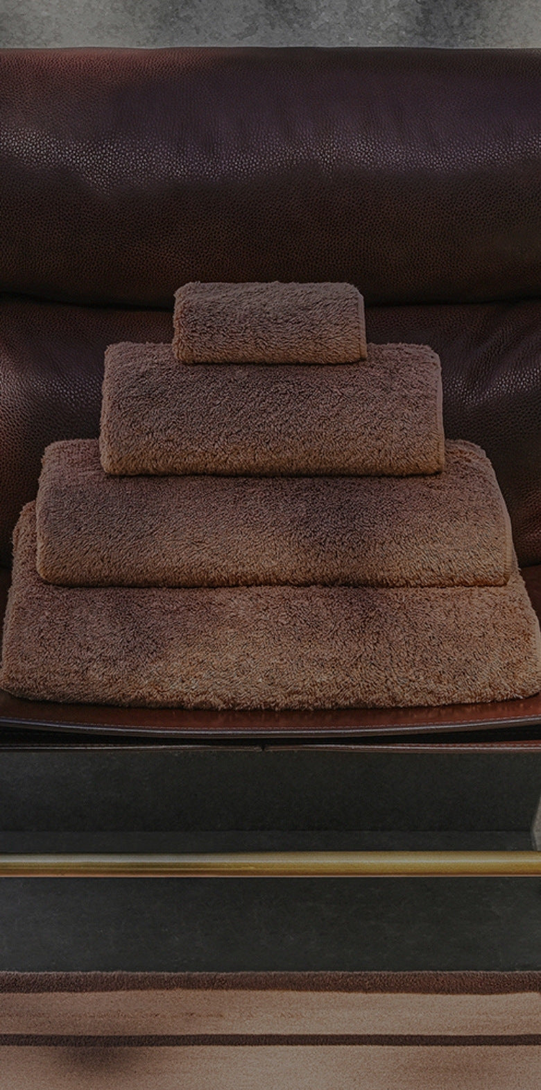 Stack of cinnamon bath towels on a brown leather chair