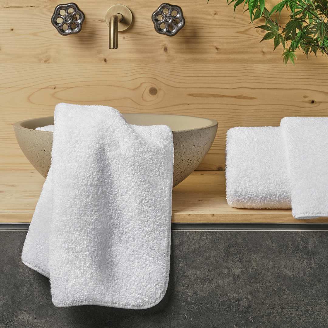 White bath towels beside a ceramic sink on a wooden bathroom counter