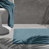 Teal bath mat on a grey floor with a matching towel over a white chair