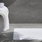 White bath mat on a gray bathroom floor with a textured wall in the background