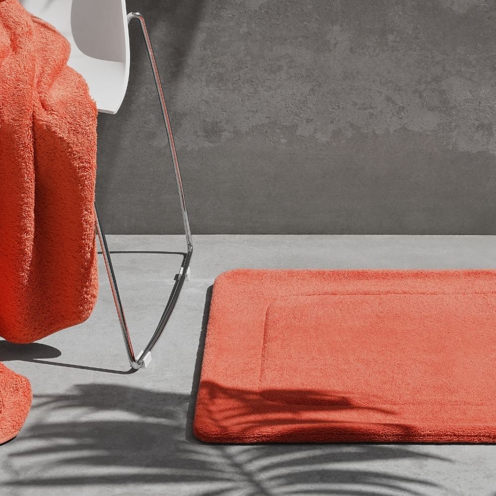 Orange bath mat on a grey floor with a matching towel over a white chair