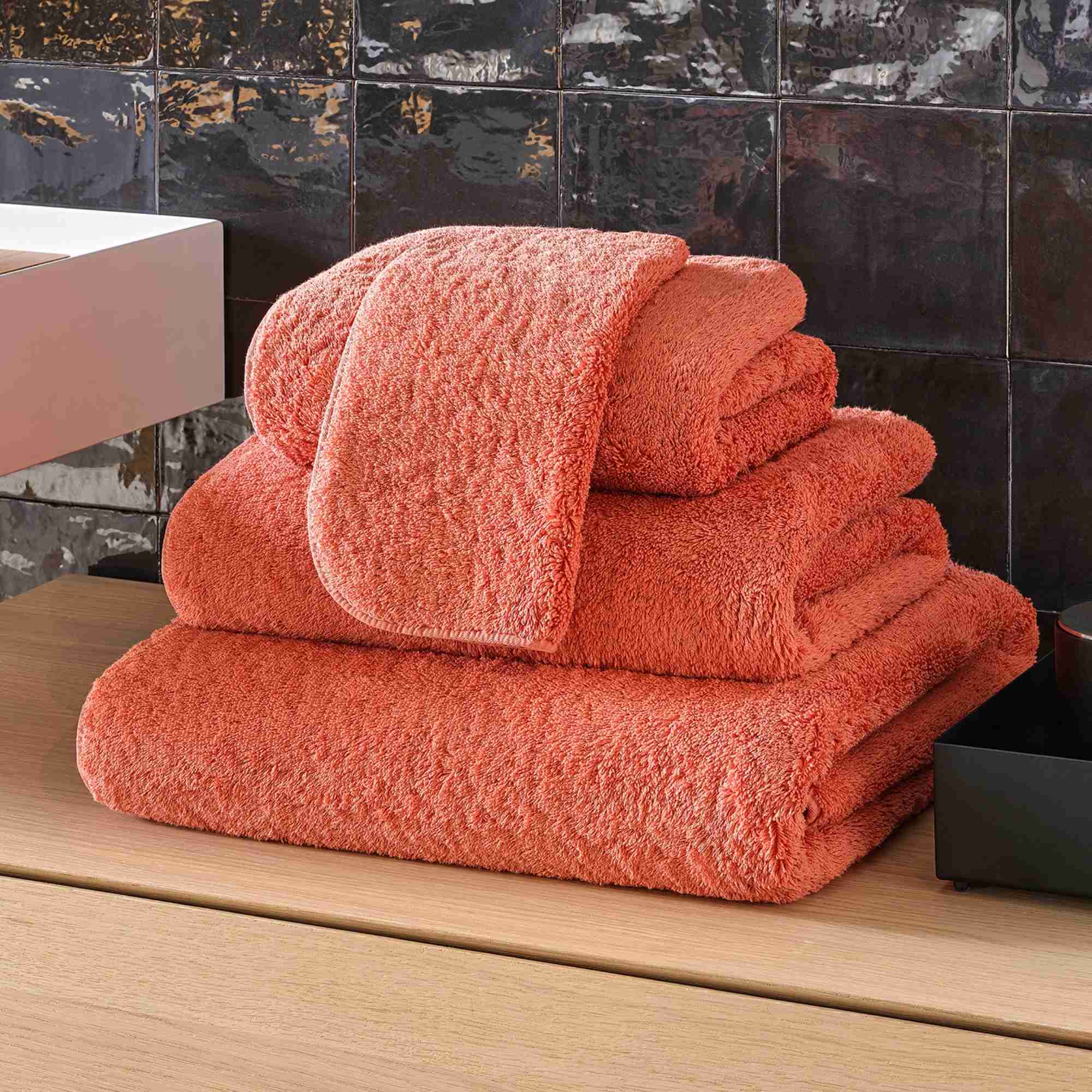 Stack of orange towels on a wooden surface with a tiled wall background