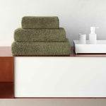 Stack of green towels on a wooden surface with a white wall background