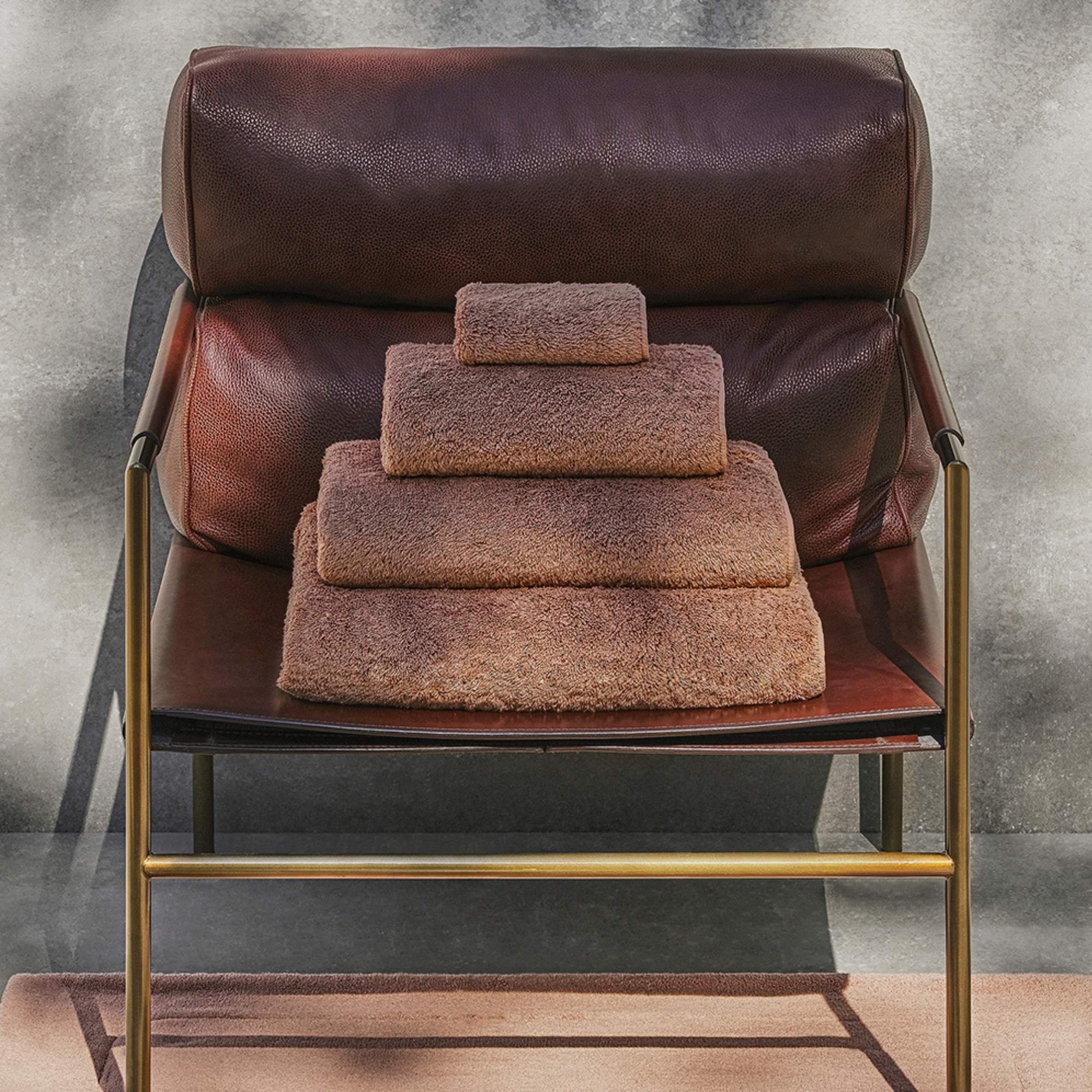 Towels stacked on a brown leather chair with a gray background
