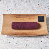 A wooden block with a purple washcloth wrapped around it on a speckled countertop.