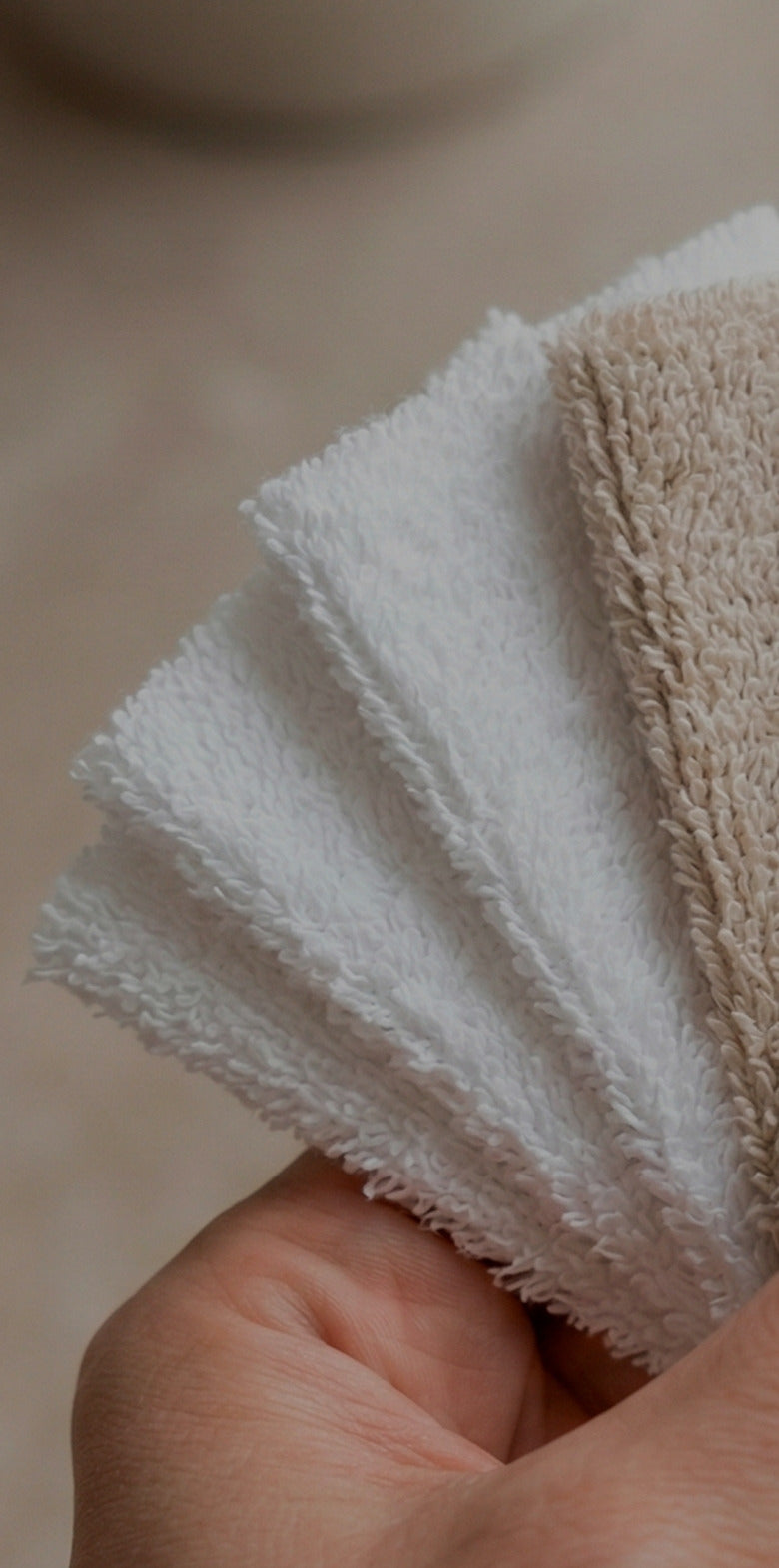 Hand holding a stack of white towels with a blurred background.